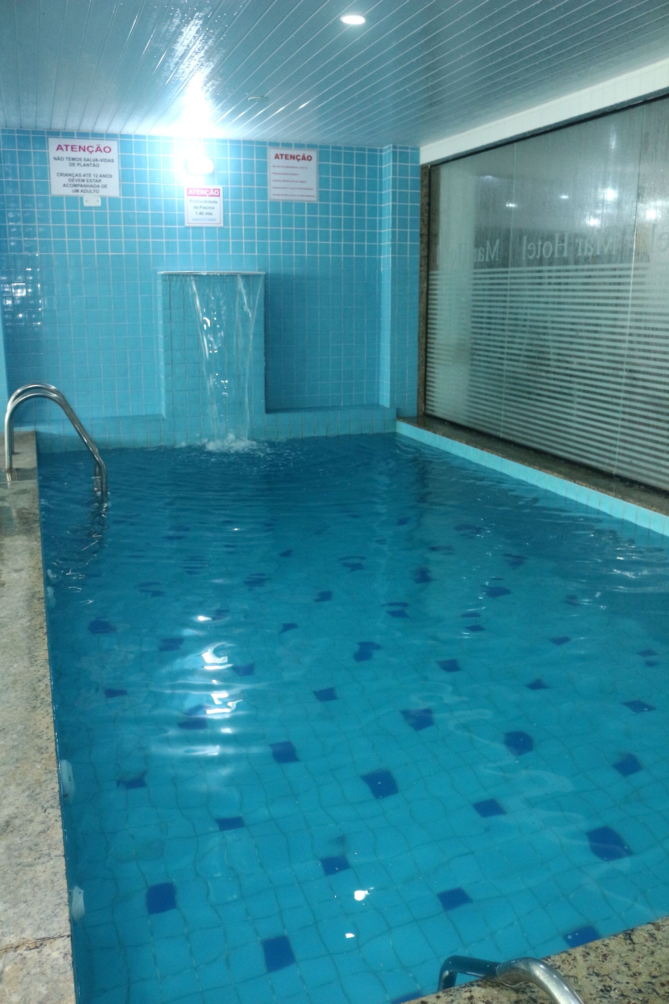 Una piscina con paredes de azulejos azules y una escalera de metal.