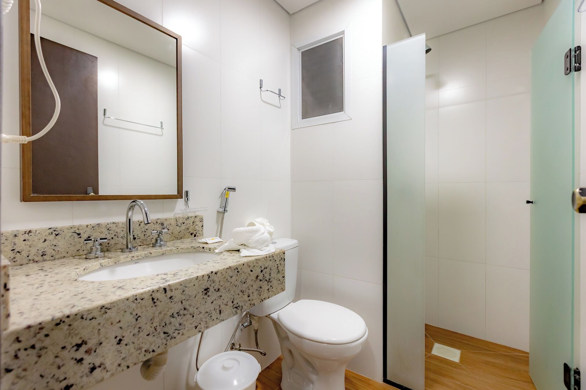 Een badkamer met een wastafelblad van graniet, een wit toilet, een douchecabine met glazen wanden en een spiegel met houten omlijsting.