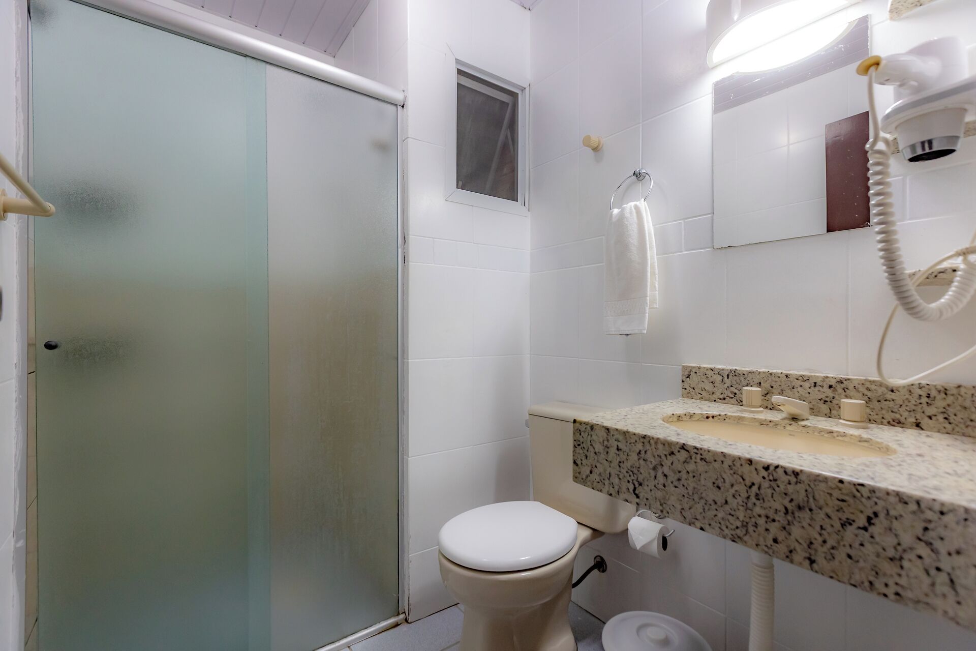 A bathroom with a toilet, a sink with a granite countertop, a mirror, and a hairdryer.