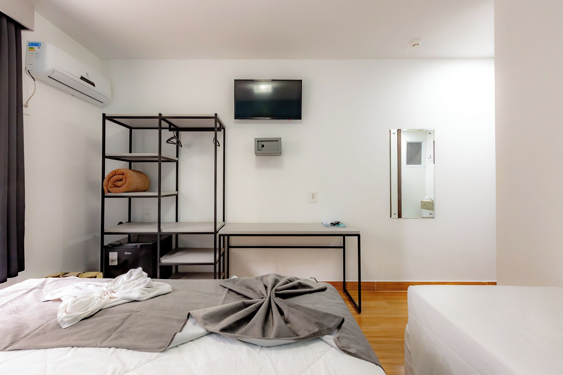 A hotel room with a bed, a desk, a TV, a wardrobe, and a mirror.
