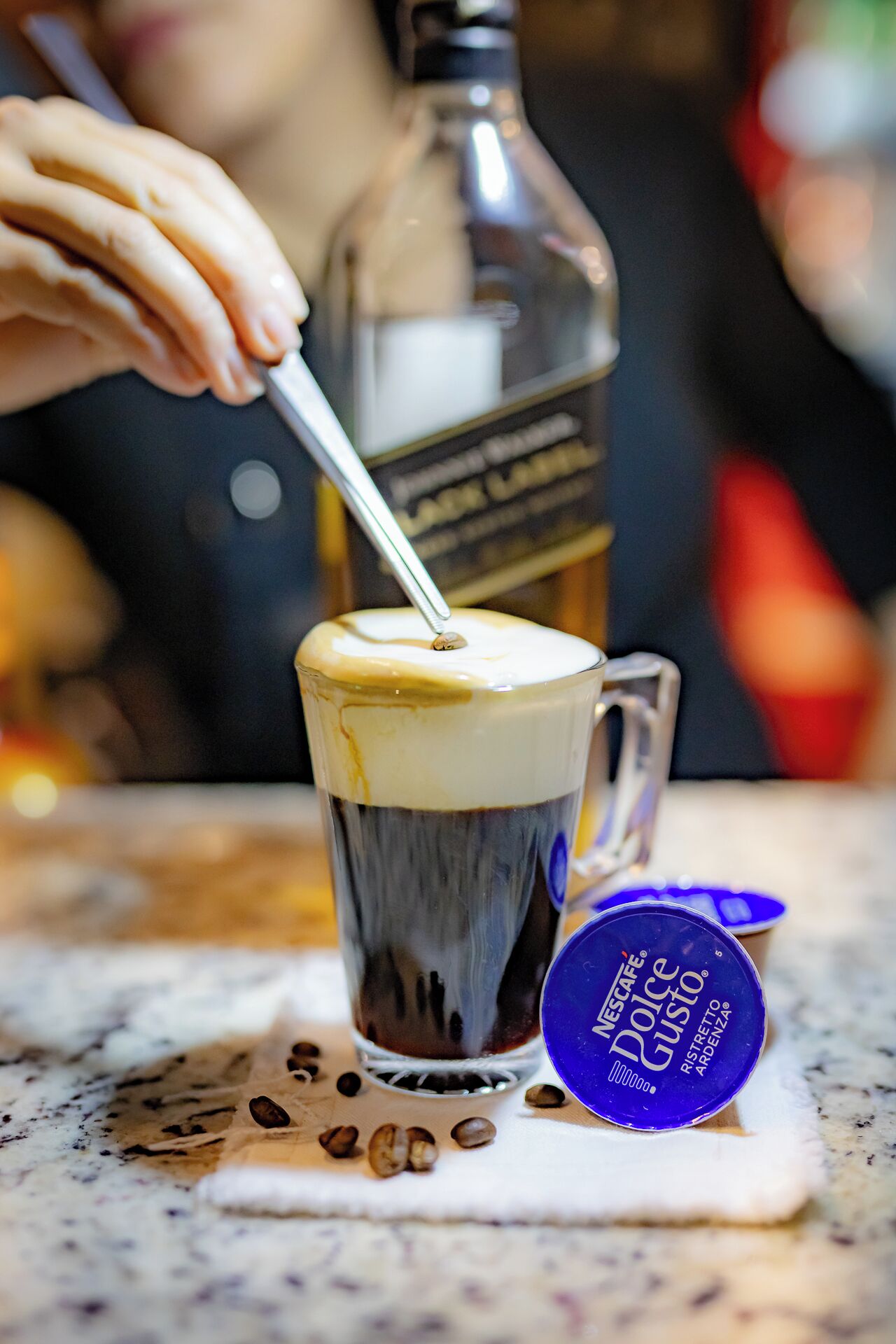 Una taza de café con una cuchara, una botella y una cápsula de café sobre una mesa.