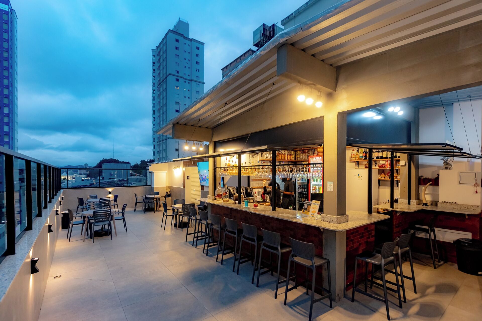 Een terras met zitplaatsen en een bar, omringd door hoge gebouwen.