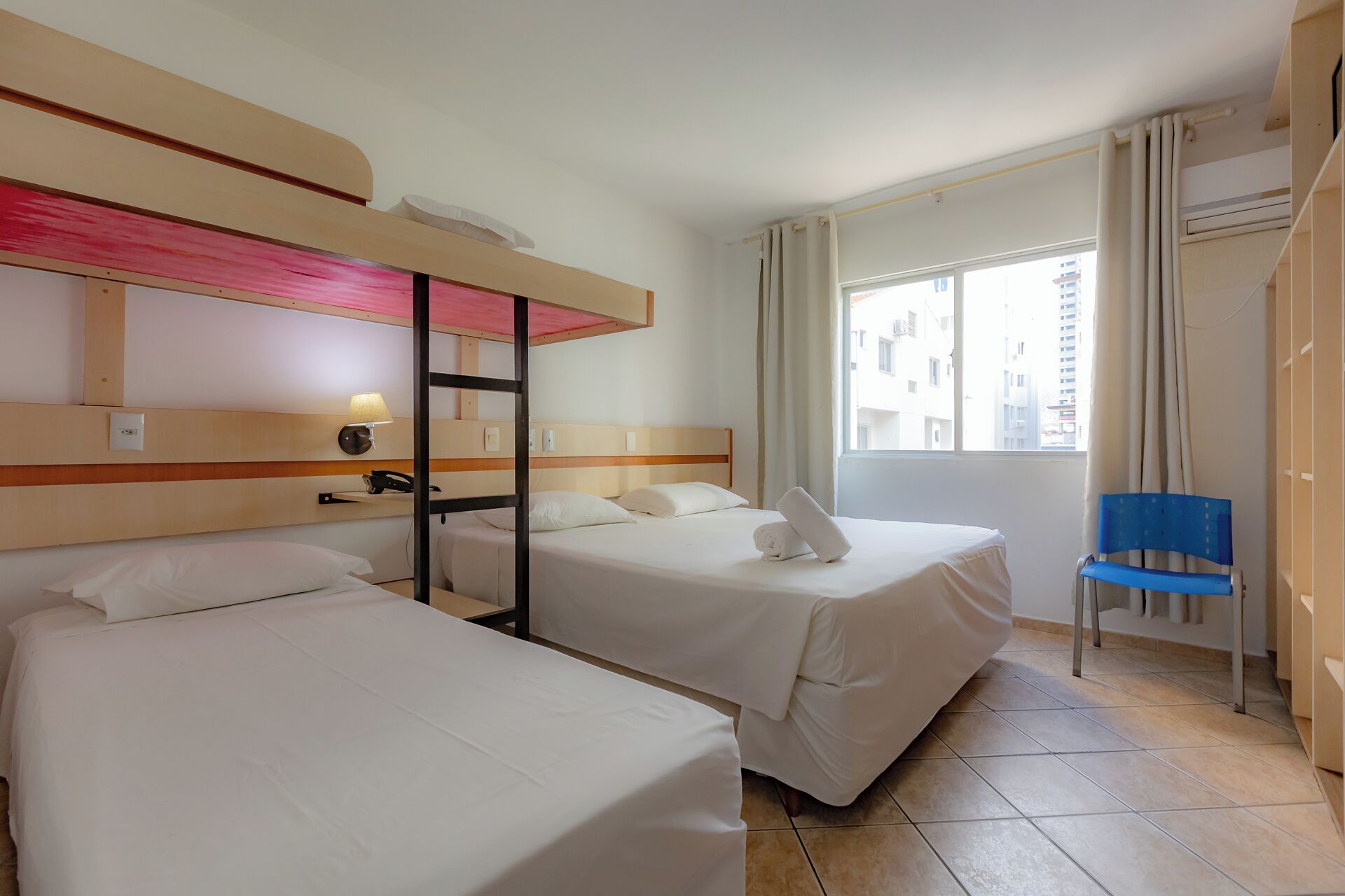 Habitación de hotel con dos camas, un escritorio, una silla y una ventana con vistas a edificios.