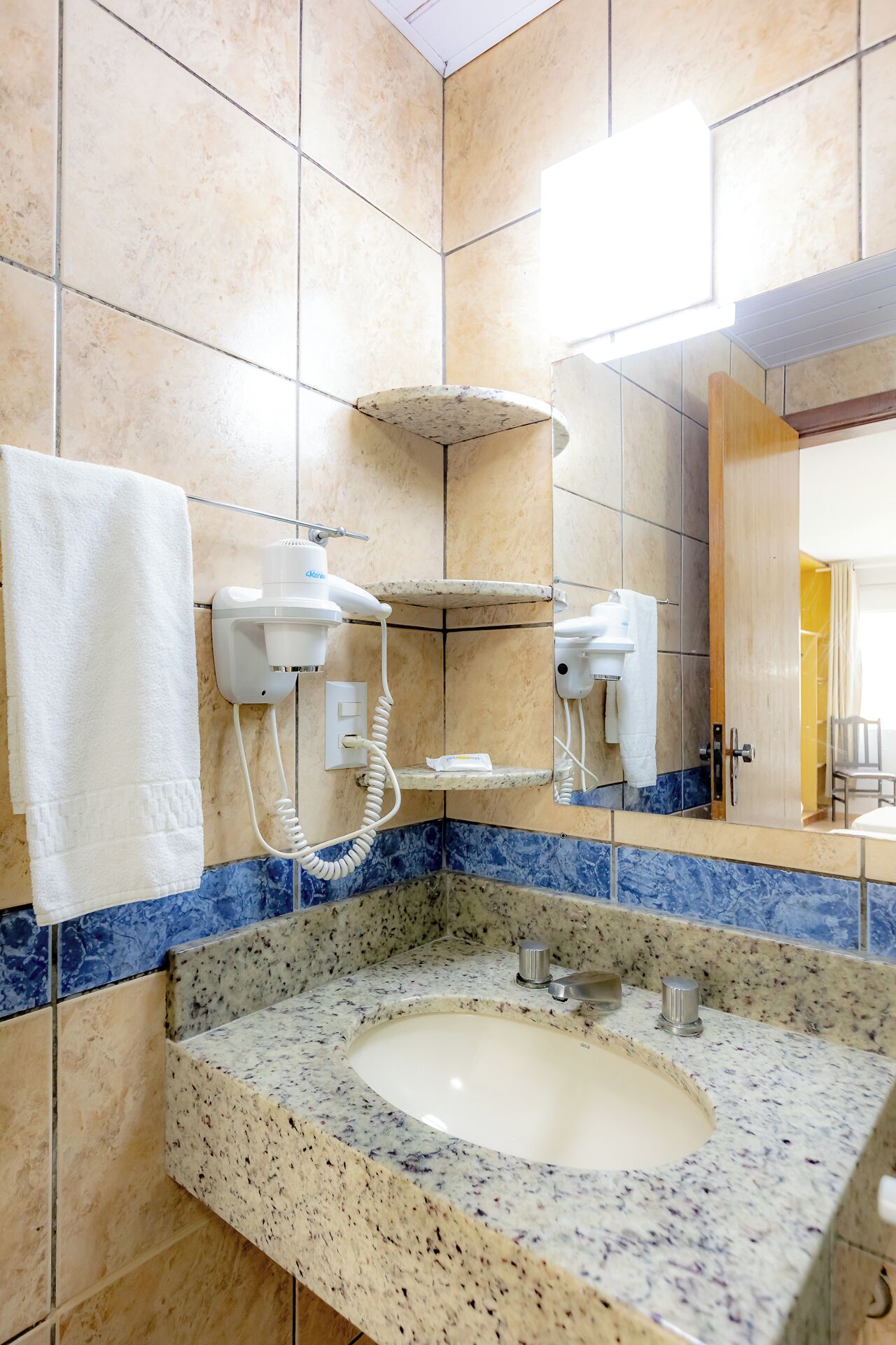 A bathroom with a granite sink, two hair dryers mounted on the wall, and a mirror above the sink.