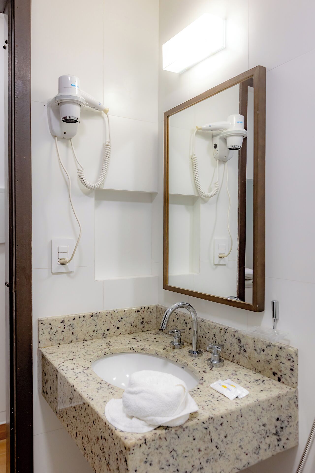 A bathroom with a granite countertop sink, a mirror, and a hairdryer mounted on the wall.