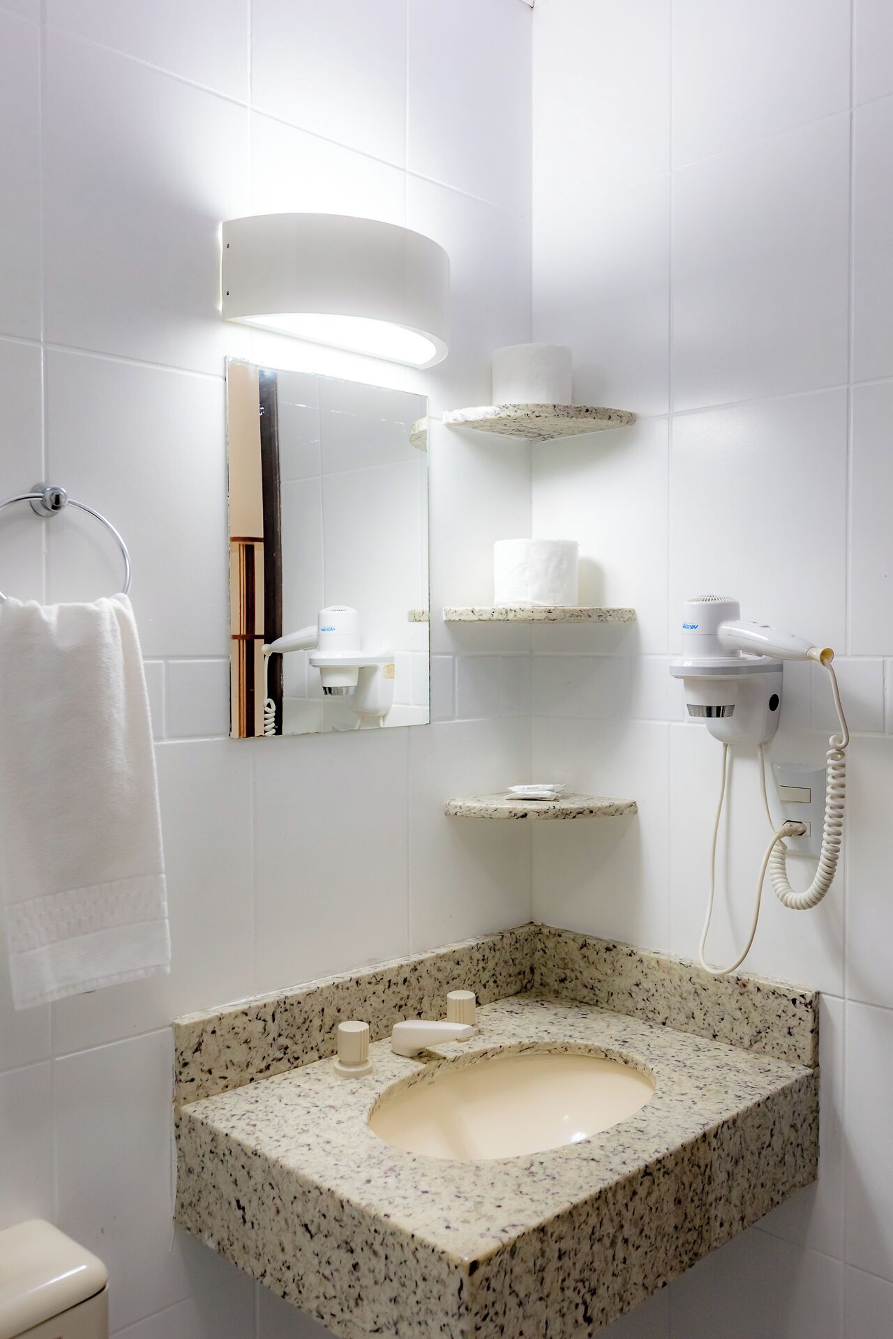 A bathroom with a granite sink, a towel rack, a mirror, and a hairdryer mounted on the wall.