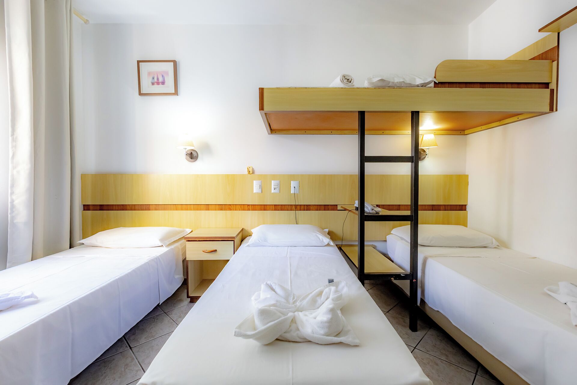 Et hotelværelse med køjesenge, et sengebord, en lampe og et billede i ramme på væggen.