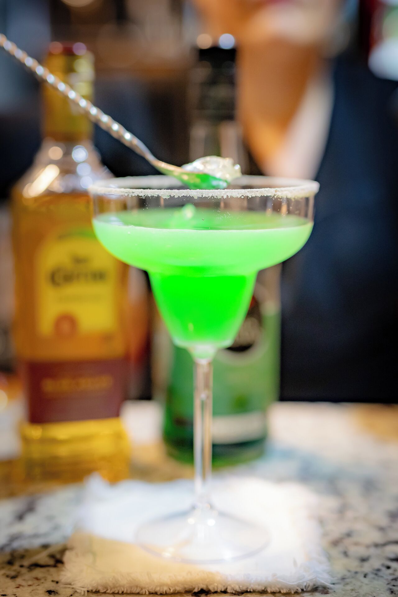 A cocktail in a martini glass with a green liquid and a rim coated with salt.