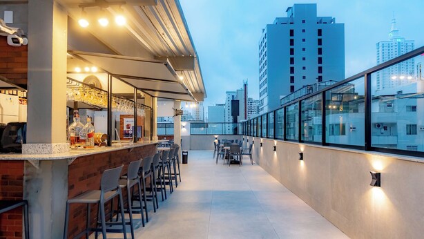Un bar en la azotea con una barra larga, varios taburetes y vistas a la ciudad.