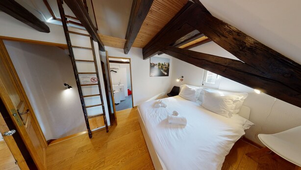 A bedroom with a wooden ceiling, a bed with white linens, a ladder, and a picture on the wall. - spacious duplex near petite france up to 4 (Strasbourg)