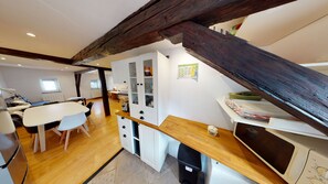 Eine kompakte Küche mit Holzbalkendecke, einer Essecke mit Tisch und Stühlen sowie ein kleiner Arbeitsbereich mit einem Computer.