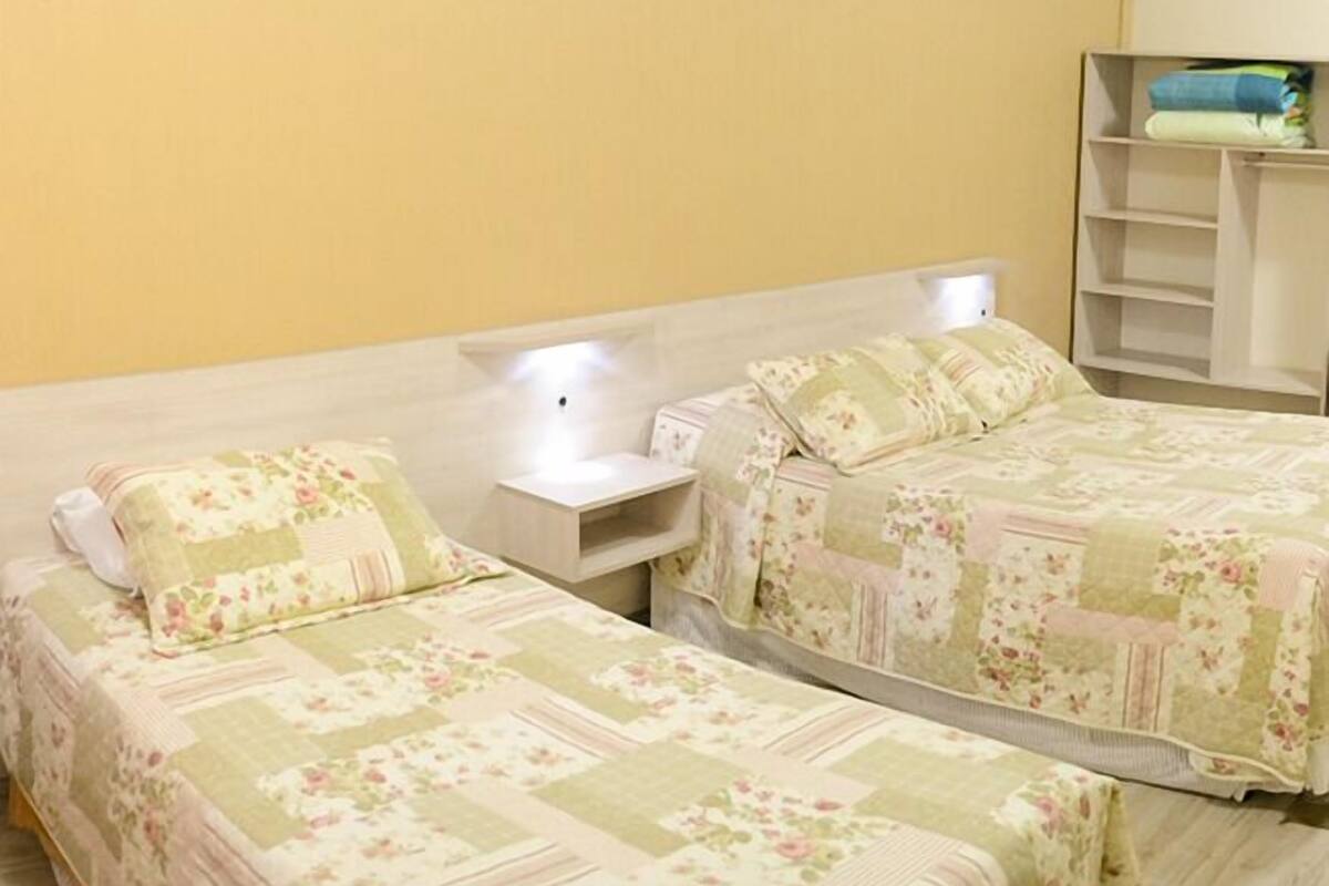Un dormitorio con dos camas, cada una con ropa de cama floral, una mesita de noche y una estantería sobre las camas.