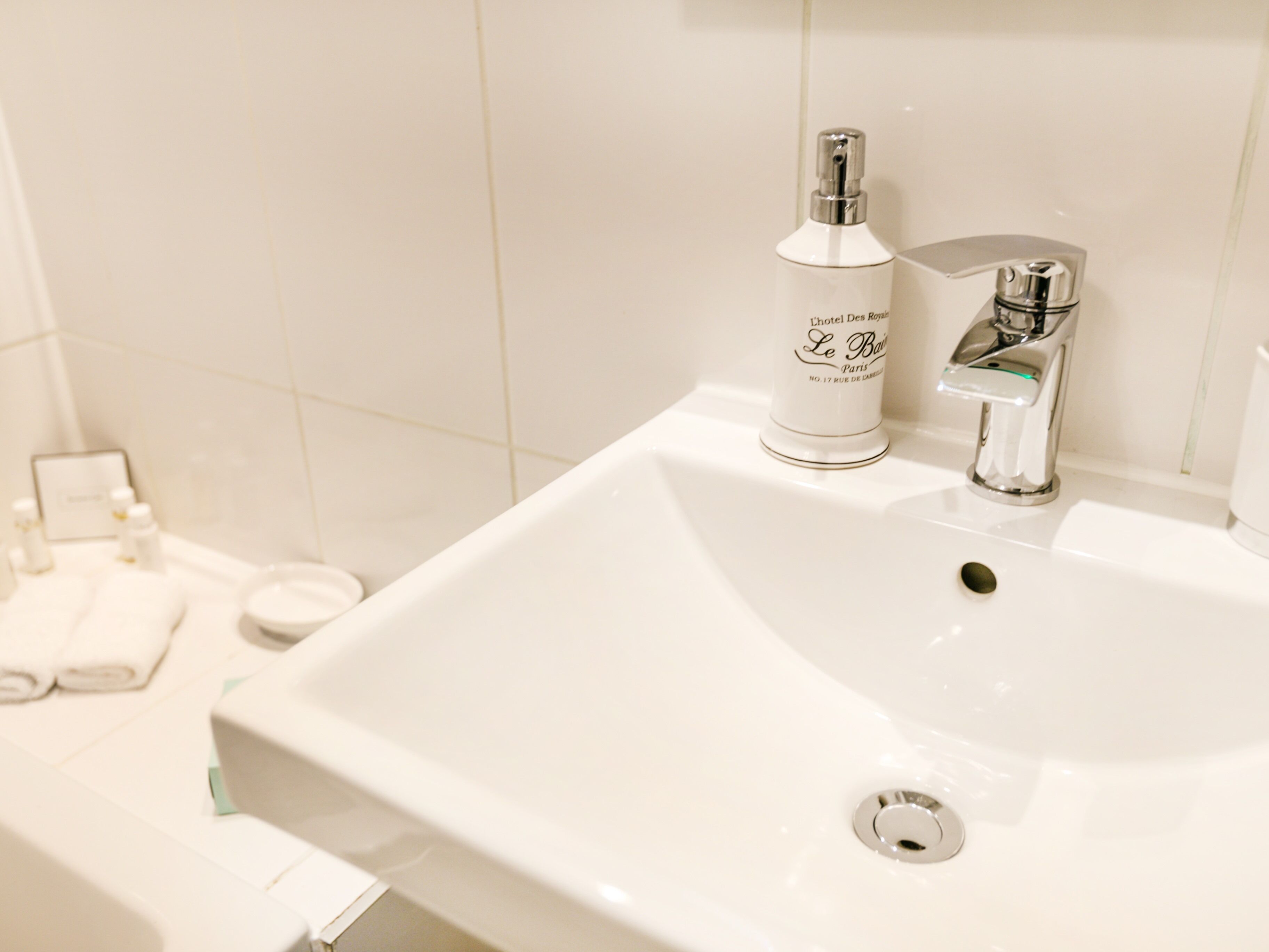 A white bathroom sink with a chrome faucet and a bottle of Le Bains Paris body wash.