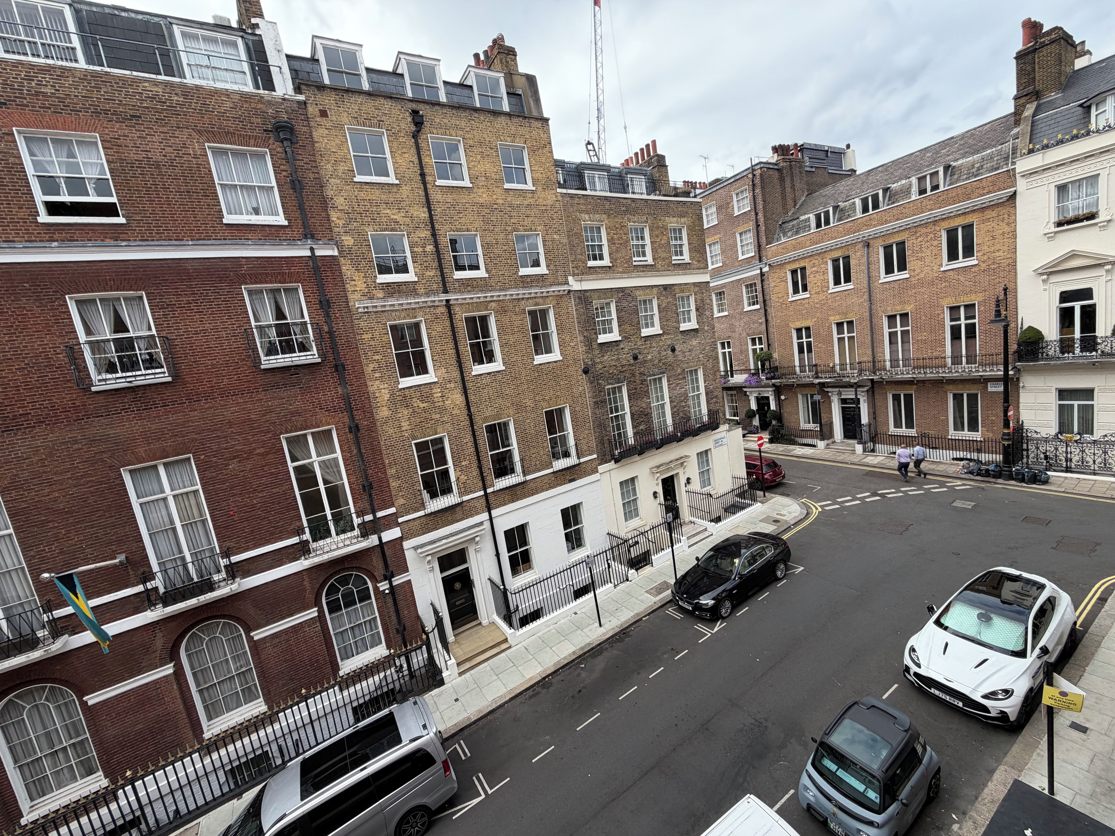 A street view with terraced houses, parked cars, and a clear sky.