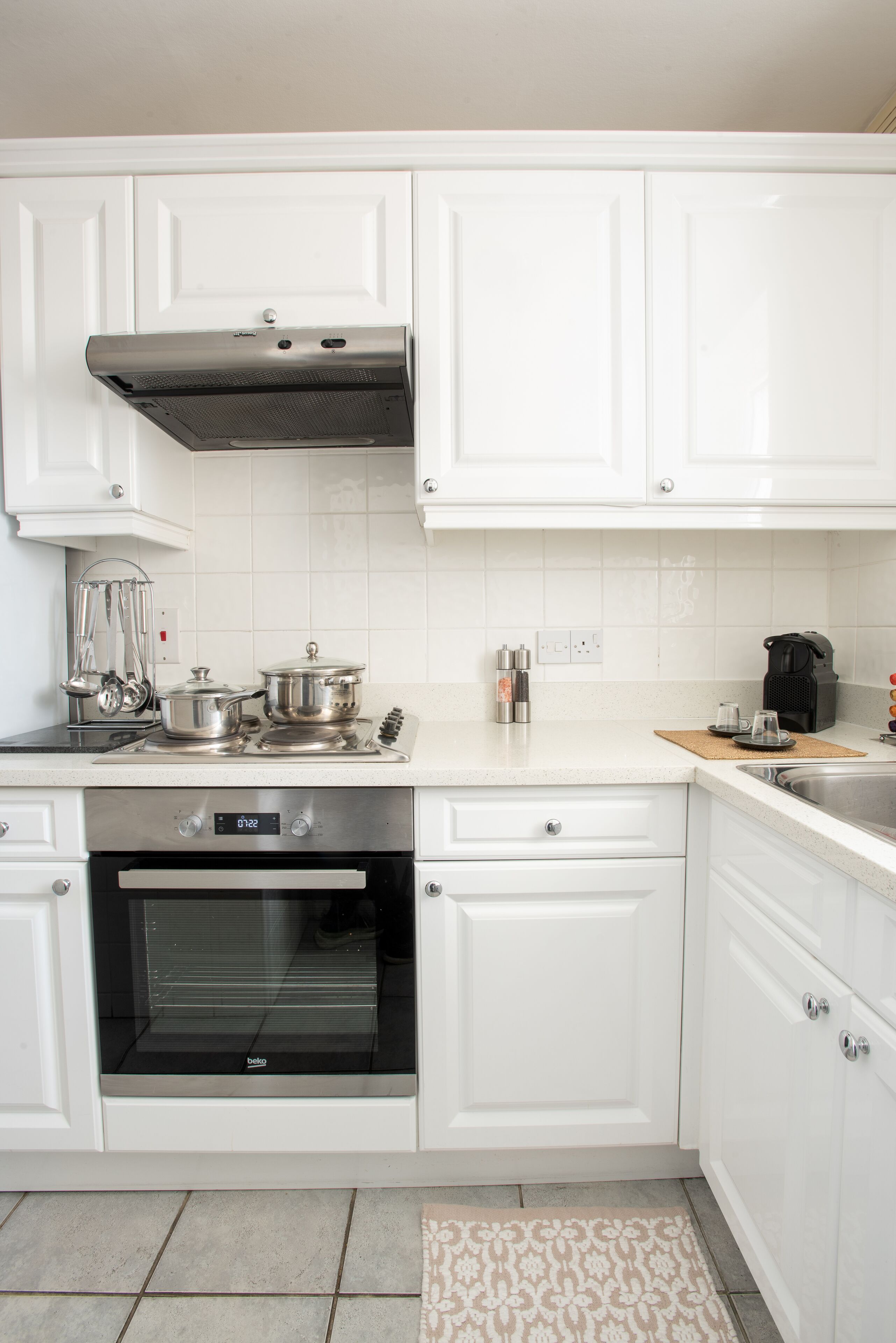 Eine moderne Küche mit weißen Schränken, einem Edelstahlbackofen und einer Kaffeemaschine.