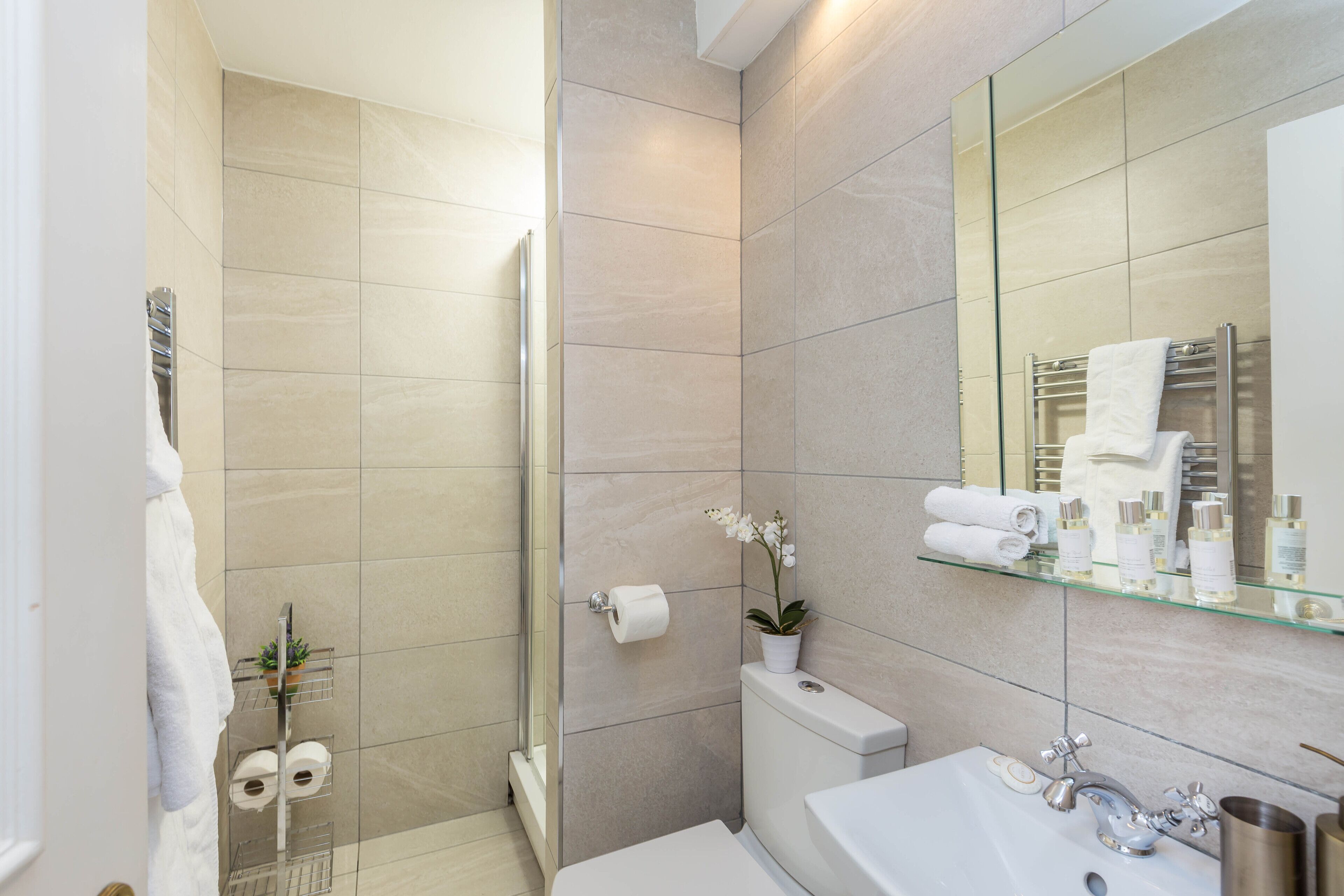Un baño moderno con ducha, inodoro y lavabo. Hay toallas y artículos de aseo en el lavabo y un espejo encima.