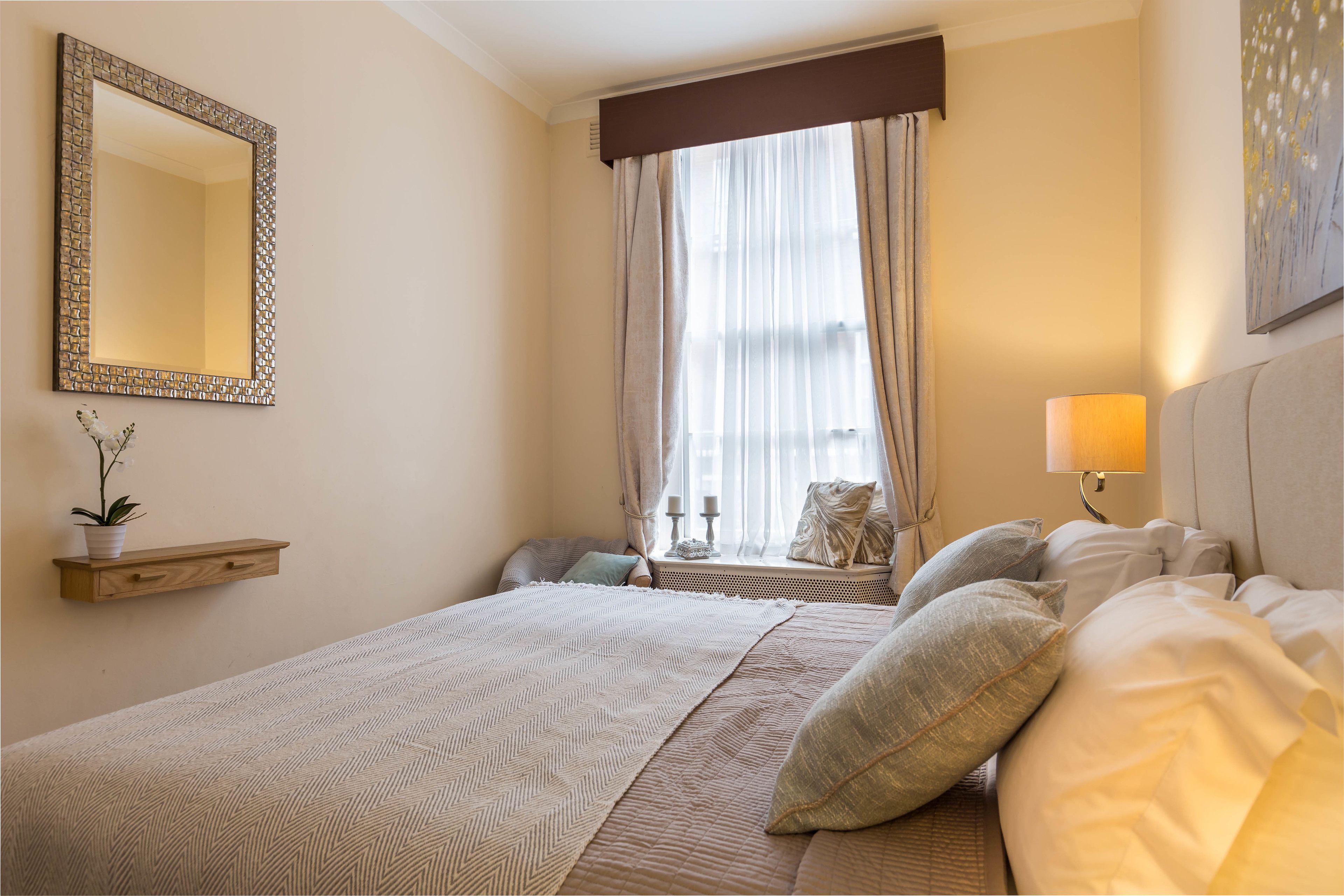 Ein Schlafzimmer mit einem großen Bett, einem Nachttisch, einem Spiegel und einem Fenster mit Vorhängen.