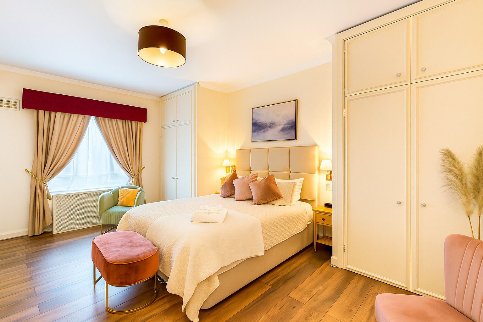 A well-lit bedroom with a bed, bedside lamps, a nightstand, a chair, and a large wardrobe.