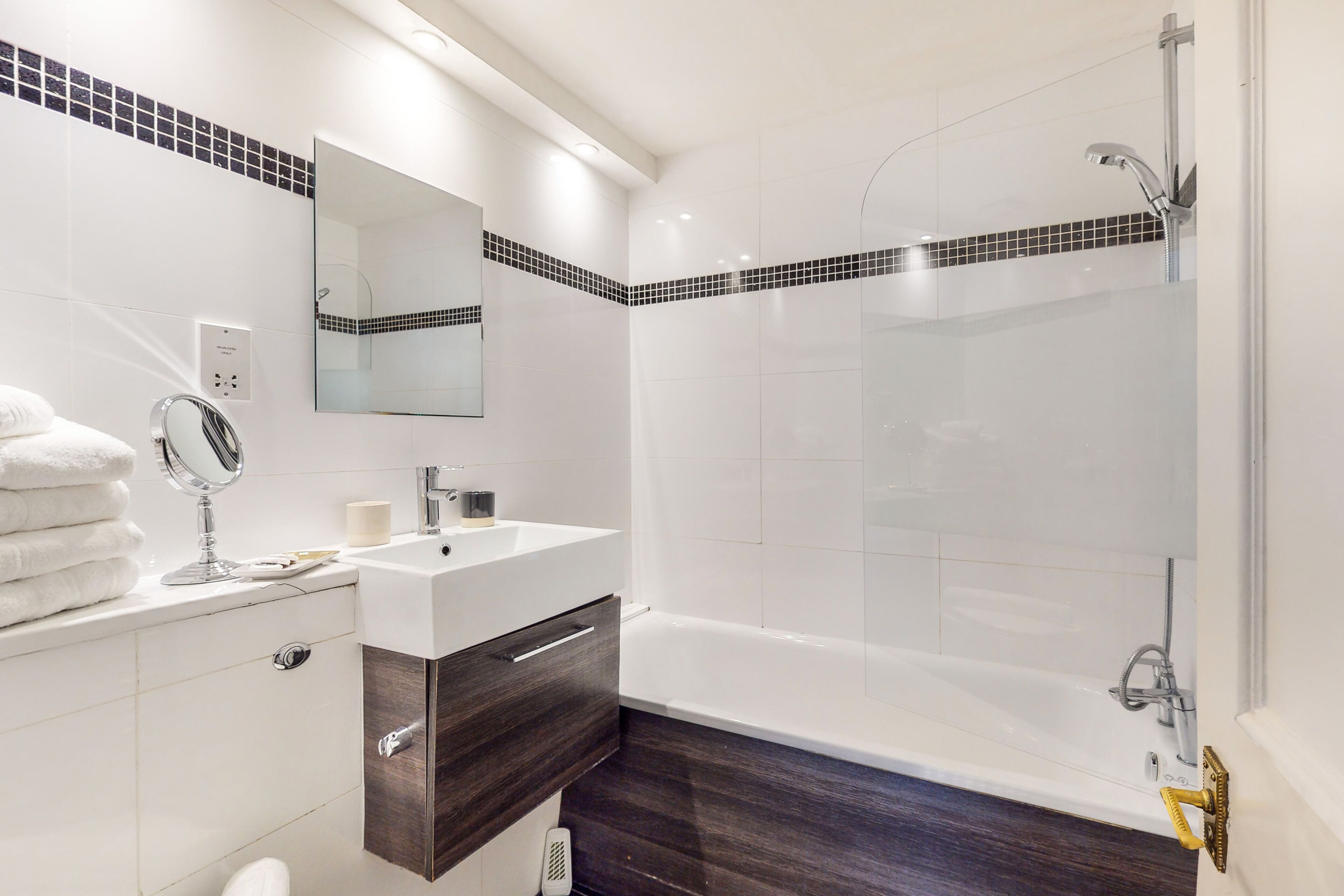 Une salle de bain moderne avec un meuble-lavabo blanc, un meuble en bois foncé, un grand miroir et une douche à parois de verre.