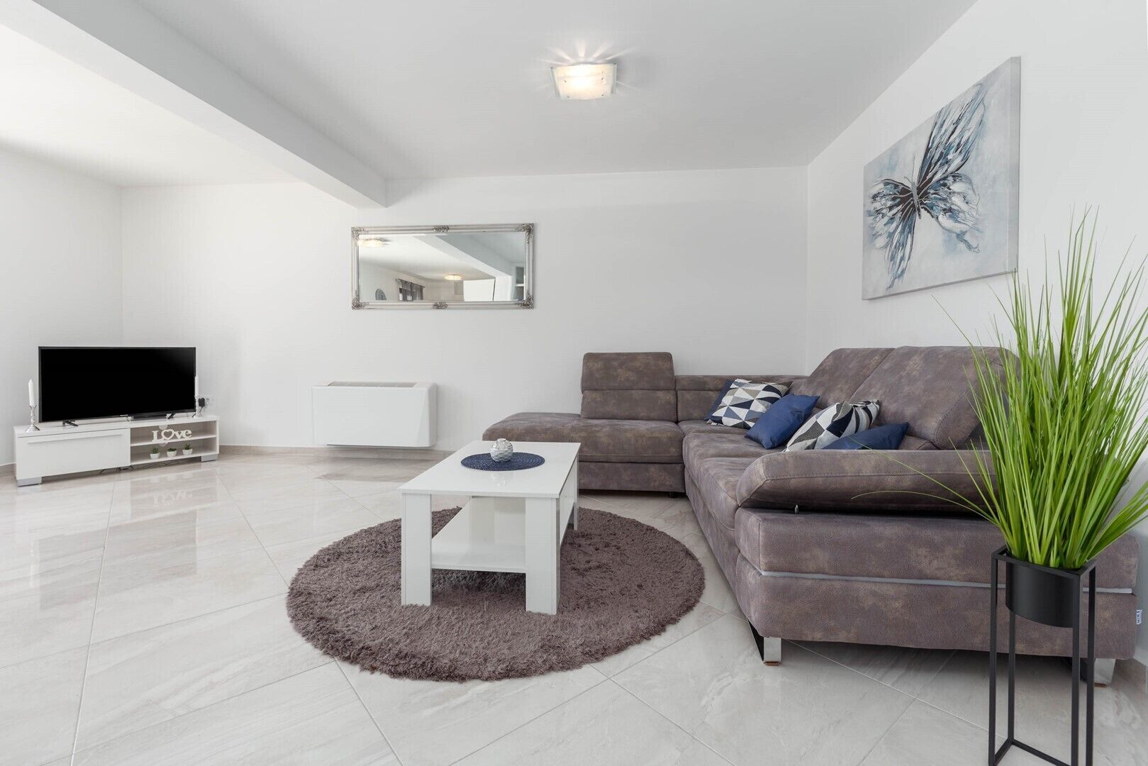 A modern living room with a flat-screen TV, a sofa, a coffee table, and a large mirror.