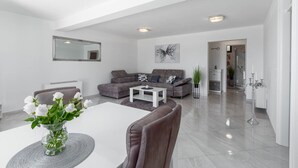 Un salon moderne avec un canapé gris, une table basse blanche et un coin repas comprenant une table et des chaises blanches.