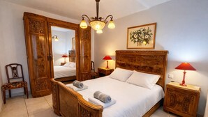 Un lit à baldaquin en bois, avec du linge de lit blanc, deux lampes de chevet, un miroir et un tableau représentant des fleurs accroché au mur.