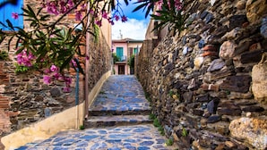 Une rue pavée bordée de murs en pierre et d’un bâtiment à la façade rose.