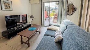 Un salon comprenant un canapé, une table basse, un téléviseur et une porte-fenêtre coulissante donnant sur une terrasse extérieure.