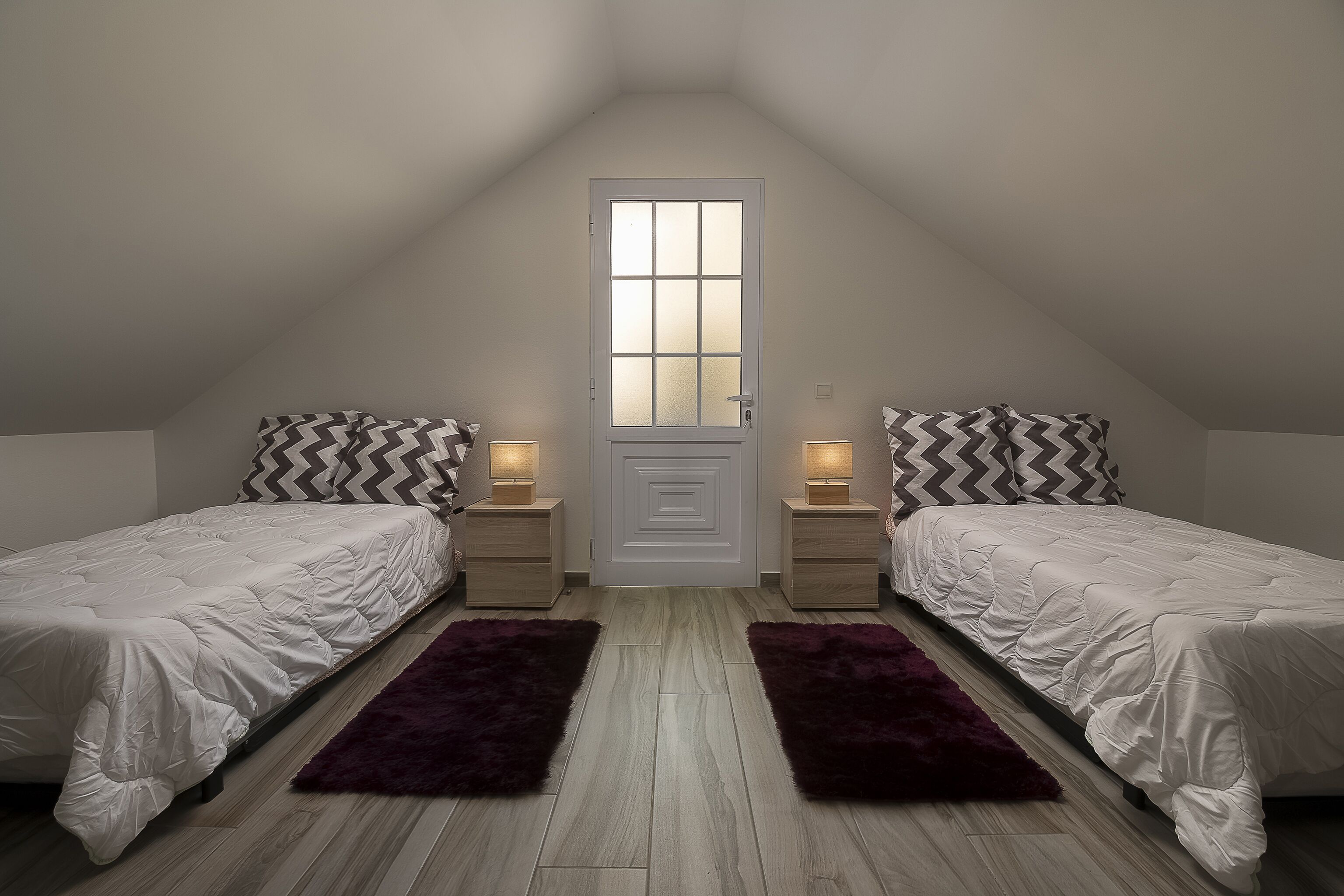 Quarto com duas camas, uma porta com painéis de vidro jateado e duas mesas de cabeceira com luminárias.