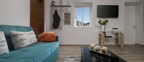 A modern living room with a teal sofa, a black coffee table, and a TV mounted on the wall.