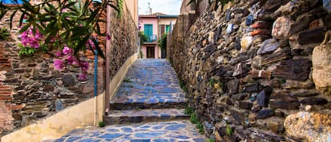 Une rue pavée bordée de murs en pierre et d’un bâtiment à la façade rose.
