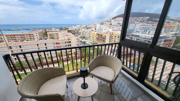 Un balcone con sedie in vimini e un tavolino, con vista su una città costiera, edifici e il mare.