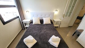 Un letto ben rifatto con due asciugamani bianchi, una coperta a letto fantasia scura e due comodini bianchi con lampade.