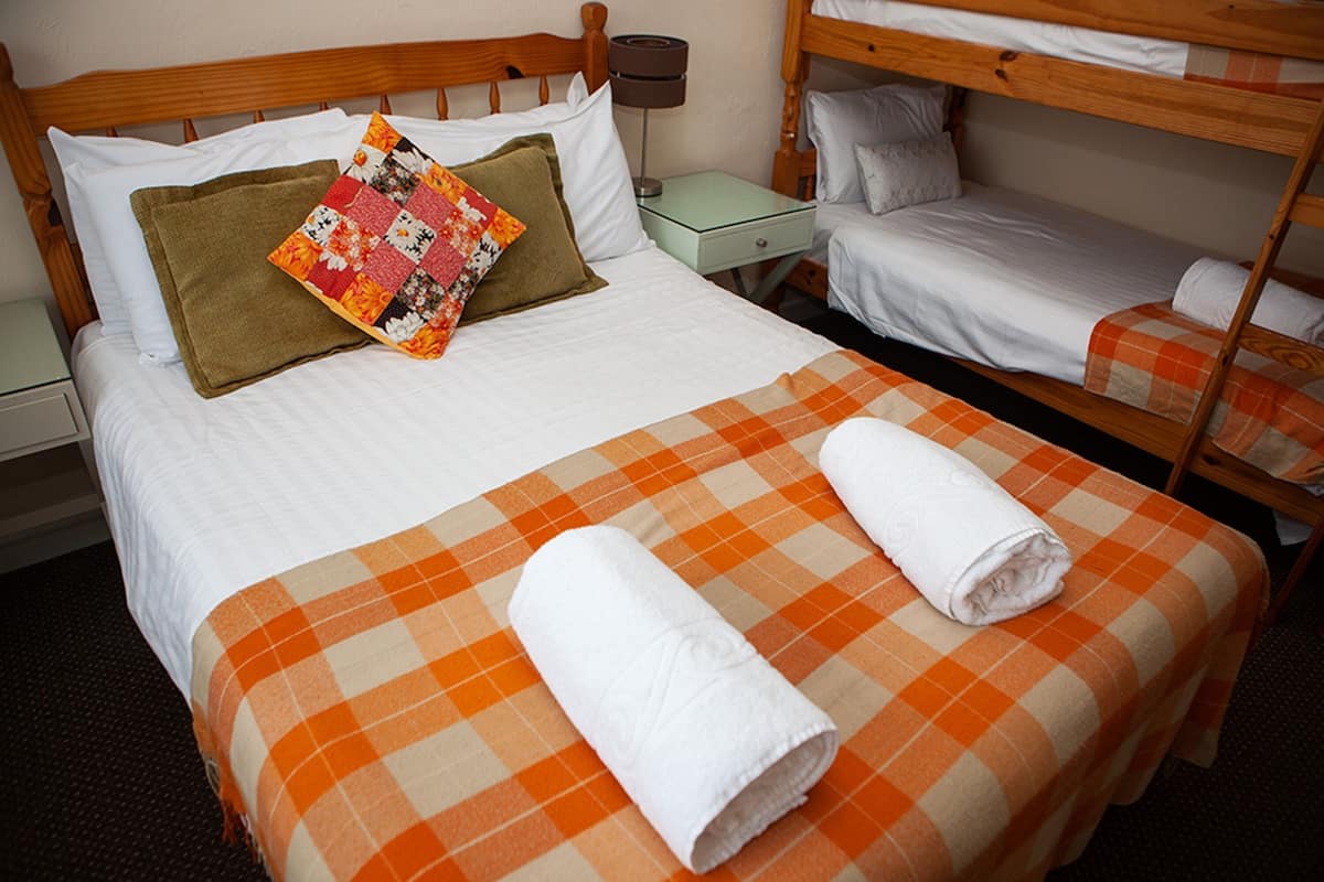 Quarto de hotel com uma cama de solteiro, mesa de cabeceira, abajur e uma beliche.