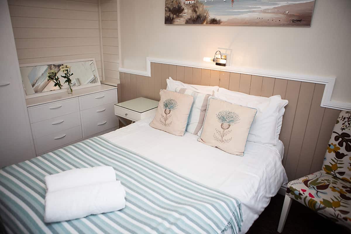 Quarto bem arrumado com uma cama, mesa de cabeceira, cômoda e uma cadeira.