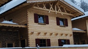 Un chalet en bois doté d’un toit à pente, de nombreuses fenêtres avec volets et d’une façade recouverte de neige.