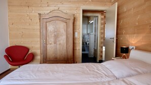 Une chambre avec une porte en bois, une chaise rouge, un lit et une table de chevet avec une lampe.