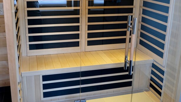 Un sauna avec des lambris en bois et des portes en verre, comprenant un banc et une plateforme surélevée.