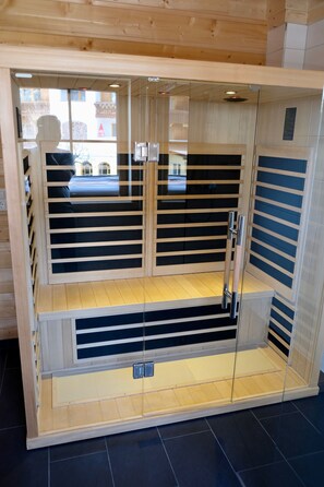A sauna with wooden slats and glass doors, featuring a bench and a lower platform. - For four: A vacation in a real log cabin—in harmony with nature (Leutasch)