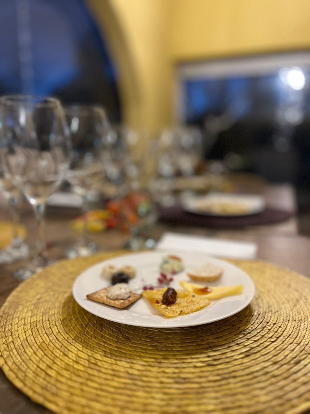 Una mesa de comedor con un plato de aperitivos, vasos y un protector de tela tejido.