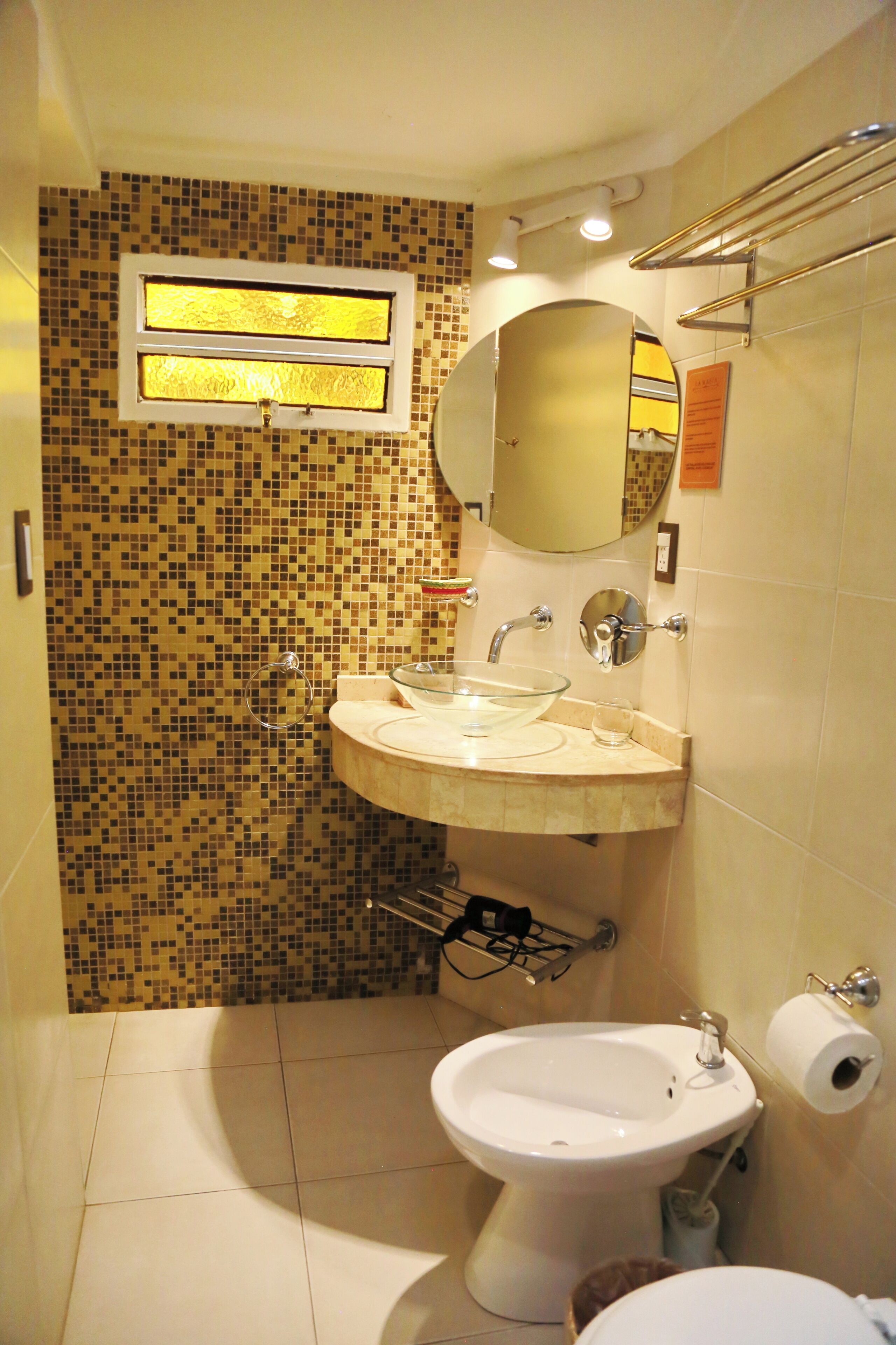 A bathroom with a mosaic tile wall, a sink with a glass bowl, a bidet, and a toilet.