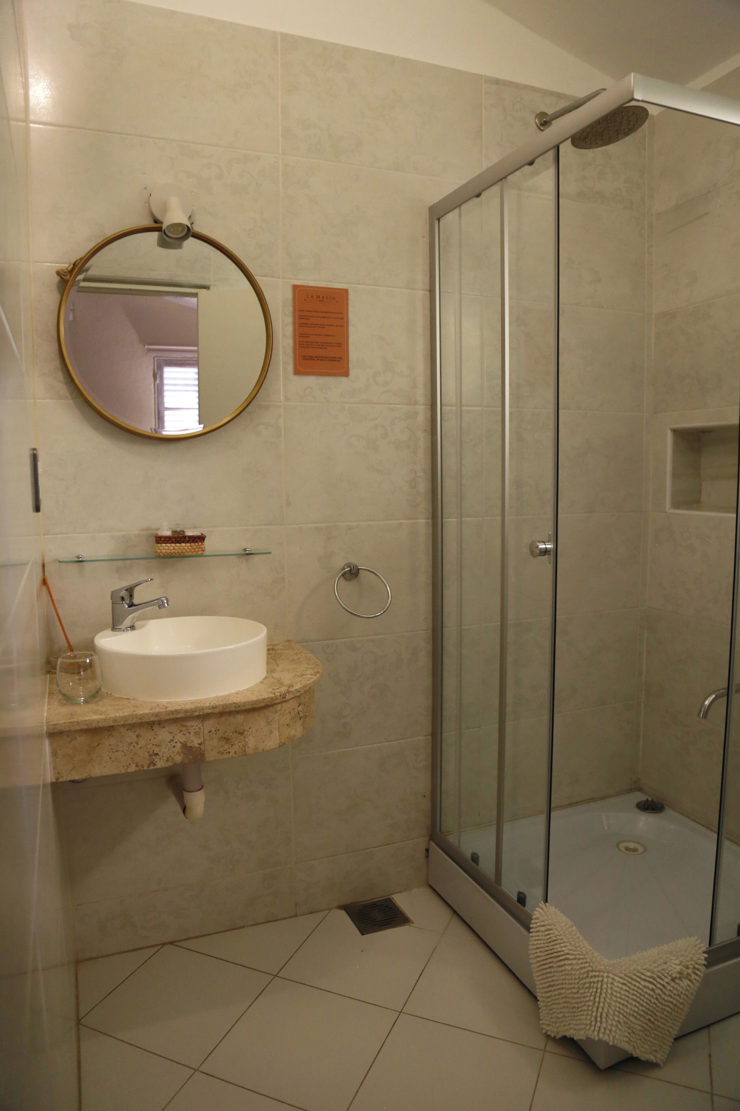 Une salle de bain avec une douche à parois de verre, un lavabo avec un miroir au-dessus et une petite étagère contenant des articles de toilette.