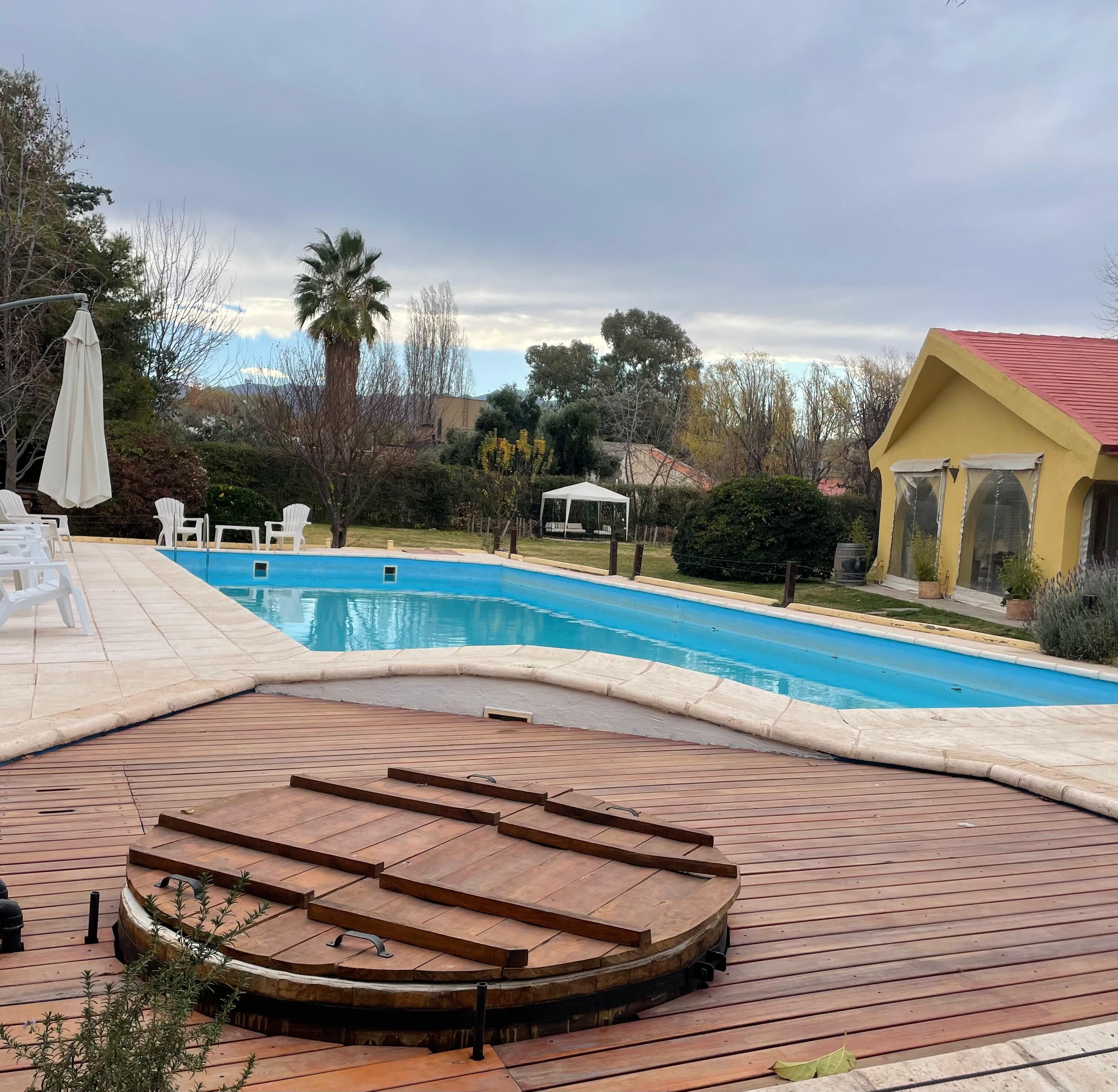 A swimming pool with a wooden deck and white chairs.