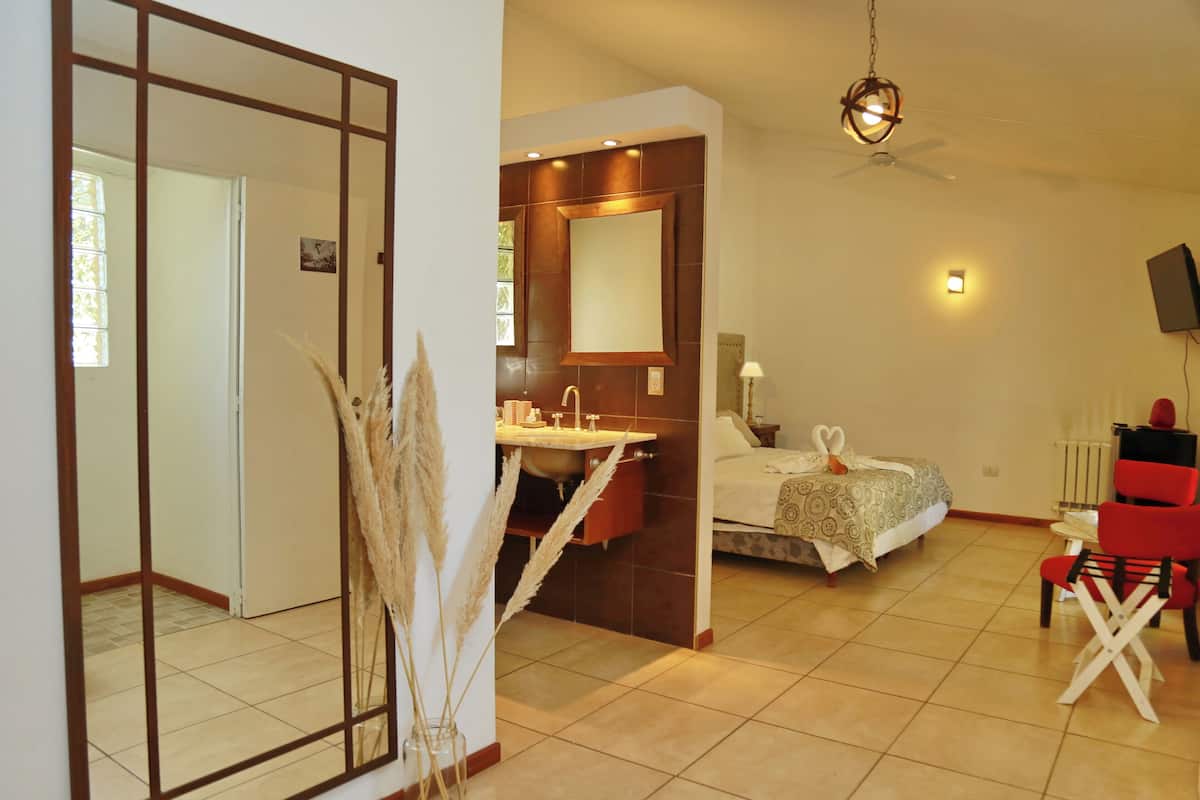 Ein Hotelzimmer mit einem großen Spiegel, einem Bett mit dekorativen Schwanenkissen, einem roten Sessel und einem Deckenventilator.