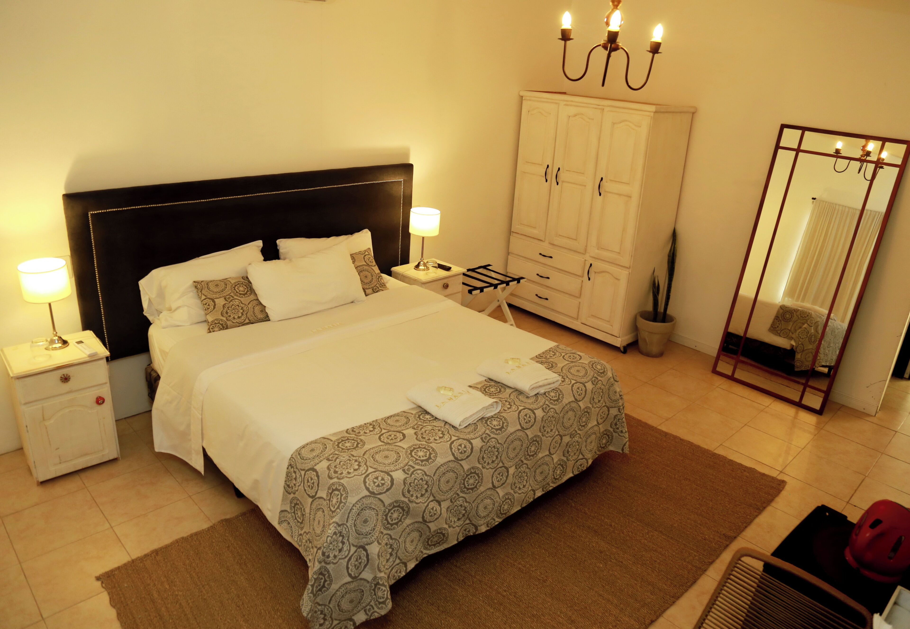 Un dormitorio ordenado con una cama grande, mesitas de noche con lámparas, un armario y un espejo.