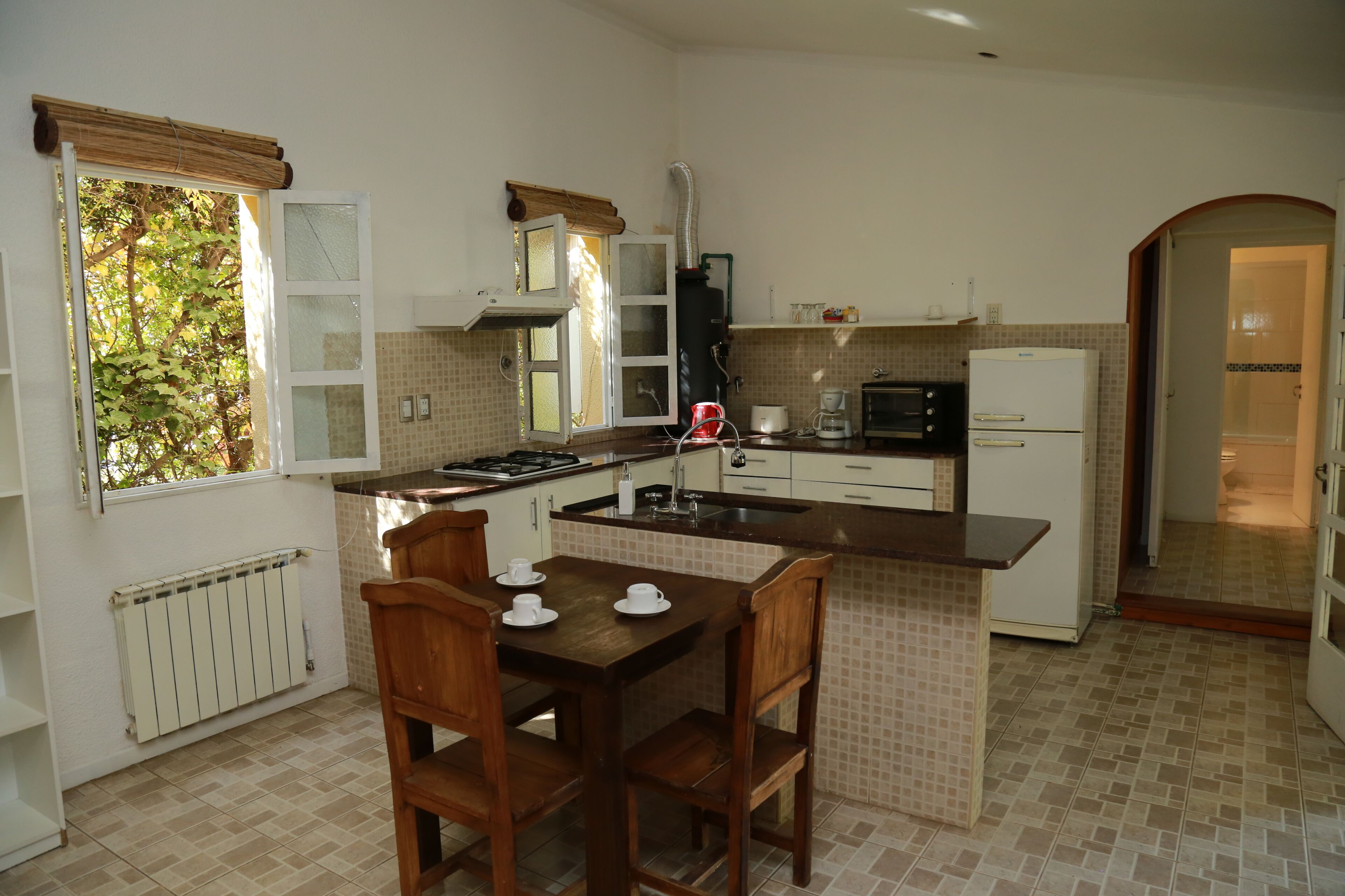 A kitchen with a dining table, chairs, a stove, a refrigerator, and a window with a view of trees.