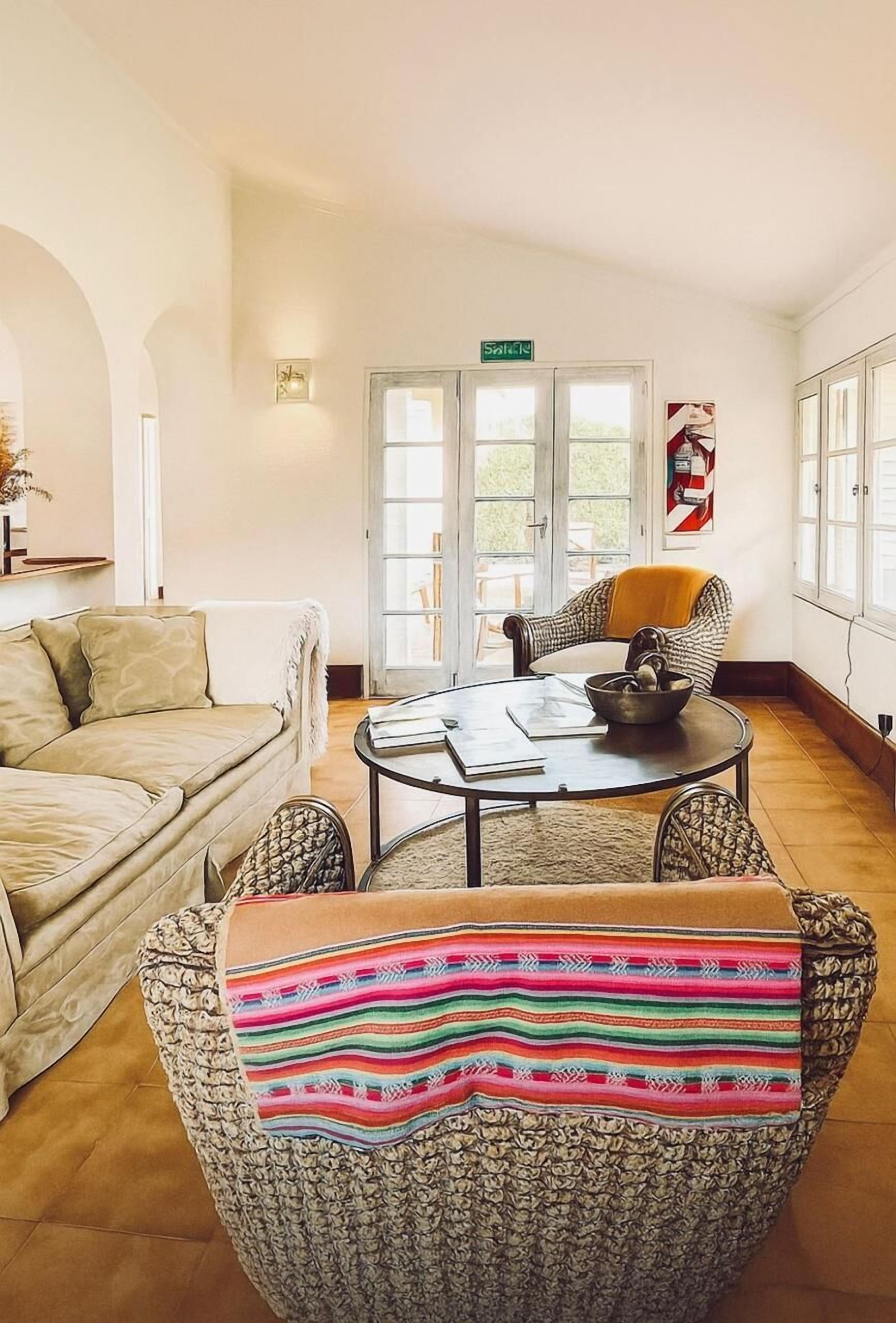 A room with a sofa, a patterned armchair, a small table with a bowl and papers, and a door with a sign.