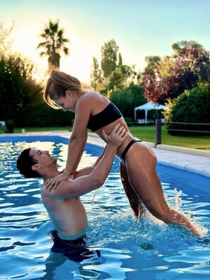 A man and a woman in a swimming pool, with trees and a white structure in the background. - La Masía Hotel Boutique (Chacras de Coria)
