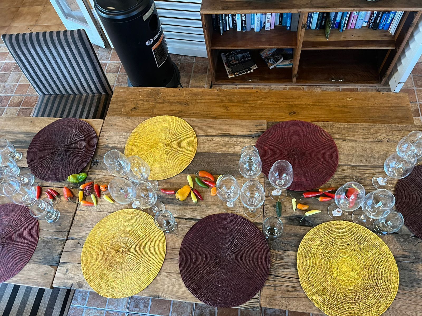A wooden table with woven placemats, clear glasses, and decorative chili peppers.