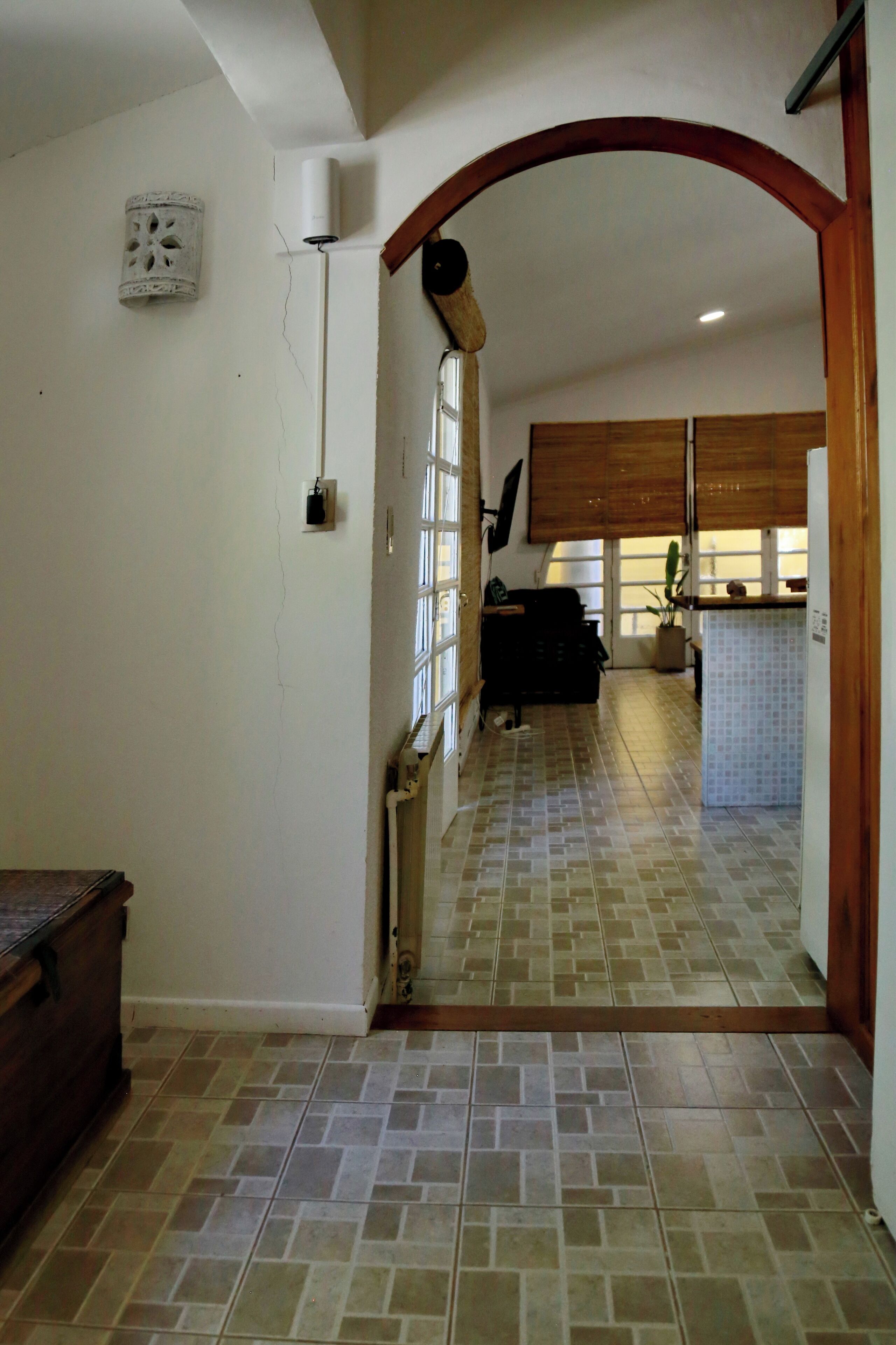 Un pasillo con piso de baldosas, un banco de madera y un acceso a una zona de cocina con salpicadero de azulejos y armarios de madera.